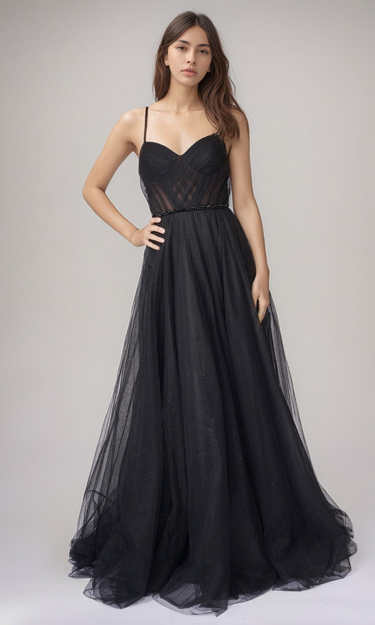 A woman poses in a studio wearing the black Nina Canacci 5401, a long formal dress with a fitted bodice and full glitter tulle skirt for an elegant sleeveless A-line look.